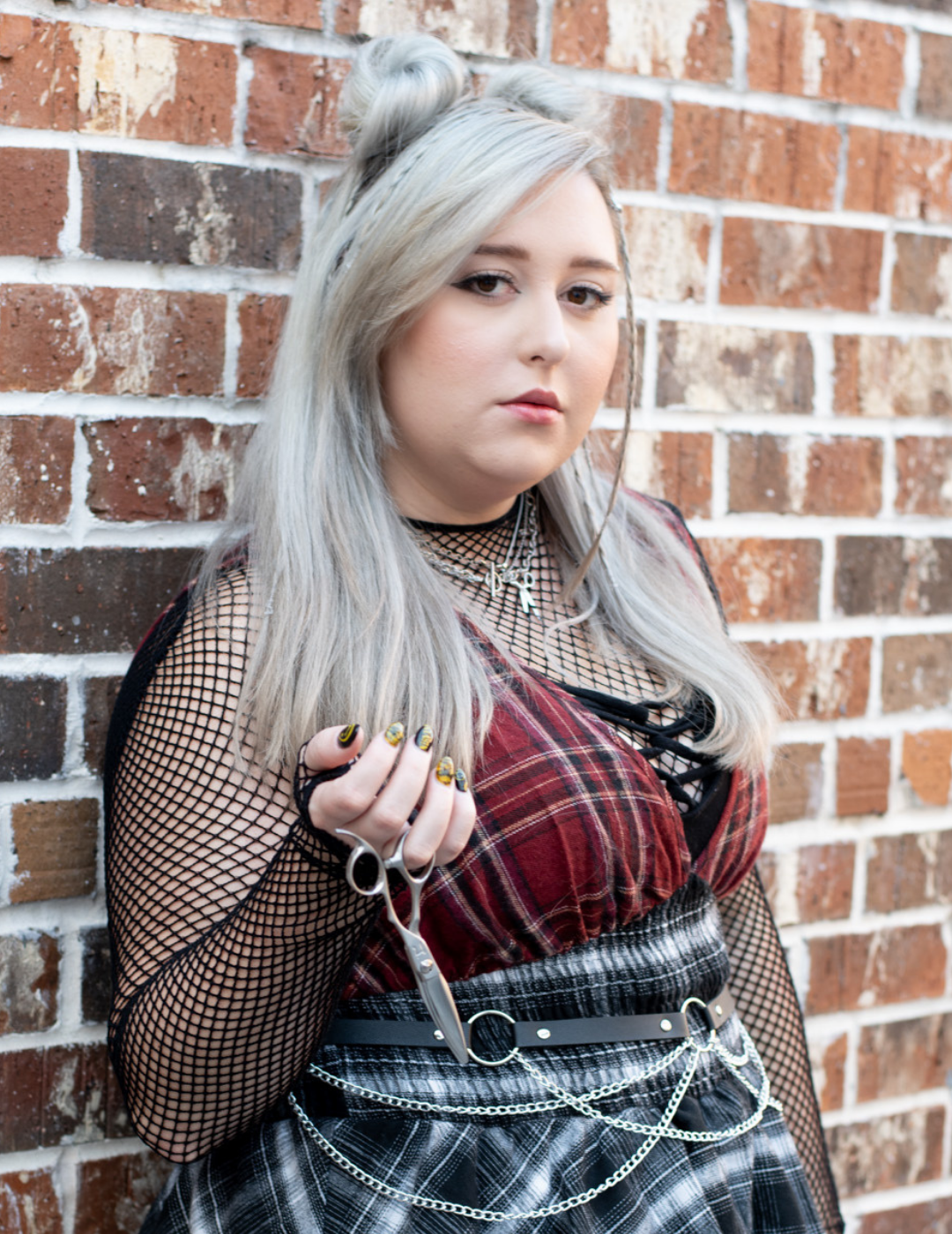 Hair stylist Cami Jasinski in Destrehan, Louisiana, with silver hair in space buns, wearing a plaid outfit and holding shears.