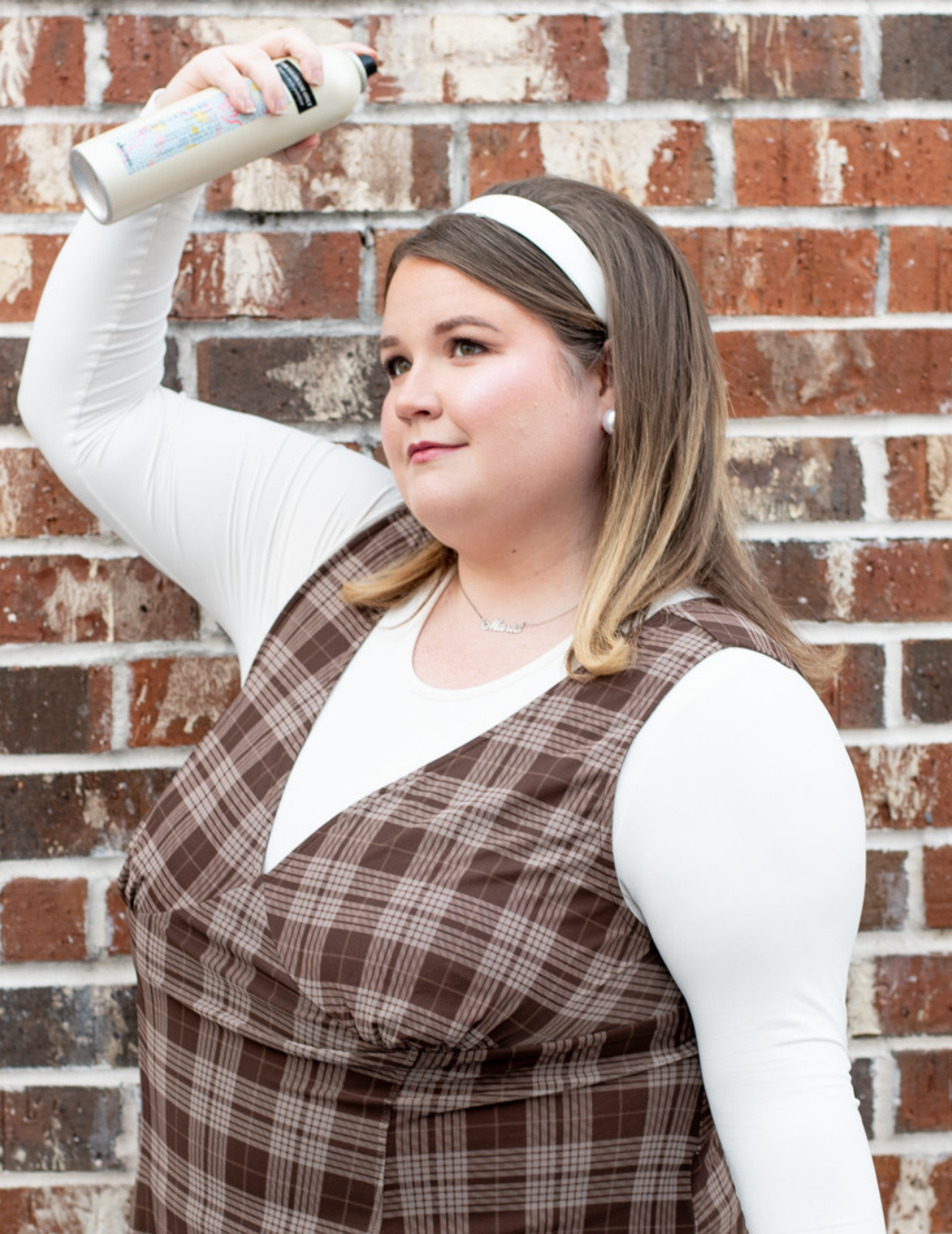 Hairstylist Marie Bourgeois in Saint Charles Parish, LA, applying hairspray to her styled hair against a brick wall.