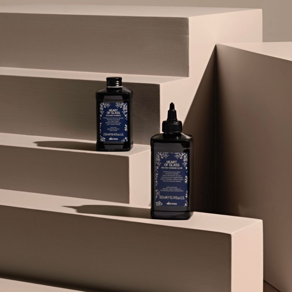 Davines Heart of Glass Silkening Shampoo and Instant Bonding Glow hair treatment for blonde hair displayed on minimalist tan pedestals in New Orleans, Louisiana.