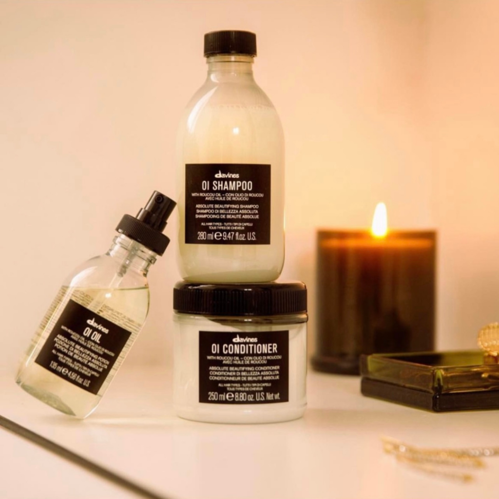 Davines OI Shampoo, Conditioner, and Oil bottles arranged on a counter with a lit candle in New Orleans.