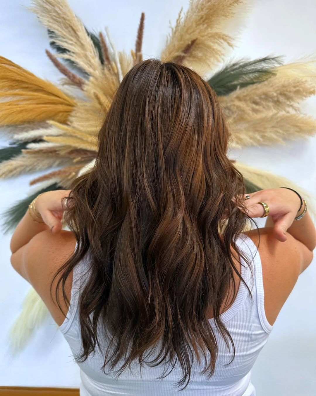 Rear view of long, wavy brunette hair with warm, dimensional light brown highlights, styled by Julia.