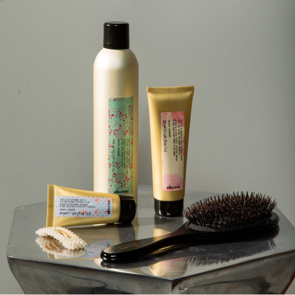 A variety of Davines More Inside hair styling products including hairspray, cream, and a hairbrush on a reflective silver surface in New Orleans, Louisiana.