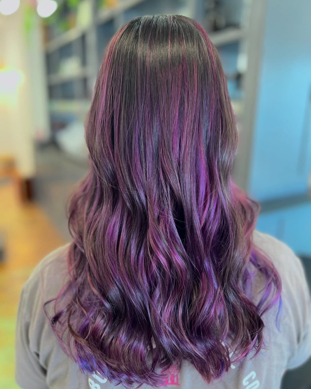 Back view of long wavy dark hair with vibrant magenta and purple highlights throughout, styled by Marie.