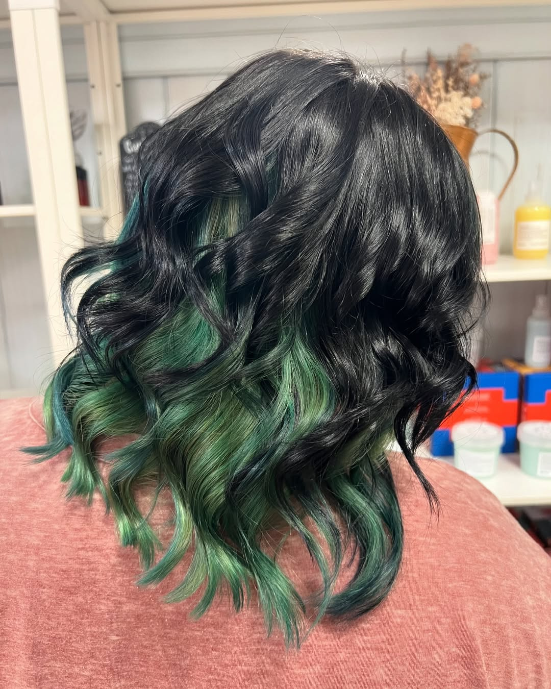 Wavy raven black hair with a vibrant forest green peek-a-boo hair color underneath, styled by Marie.