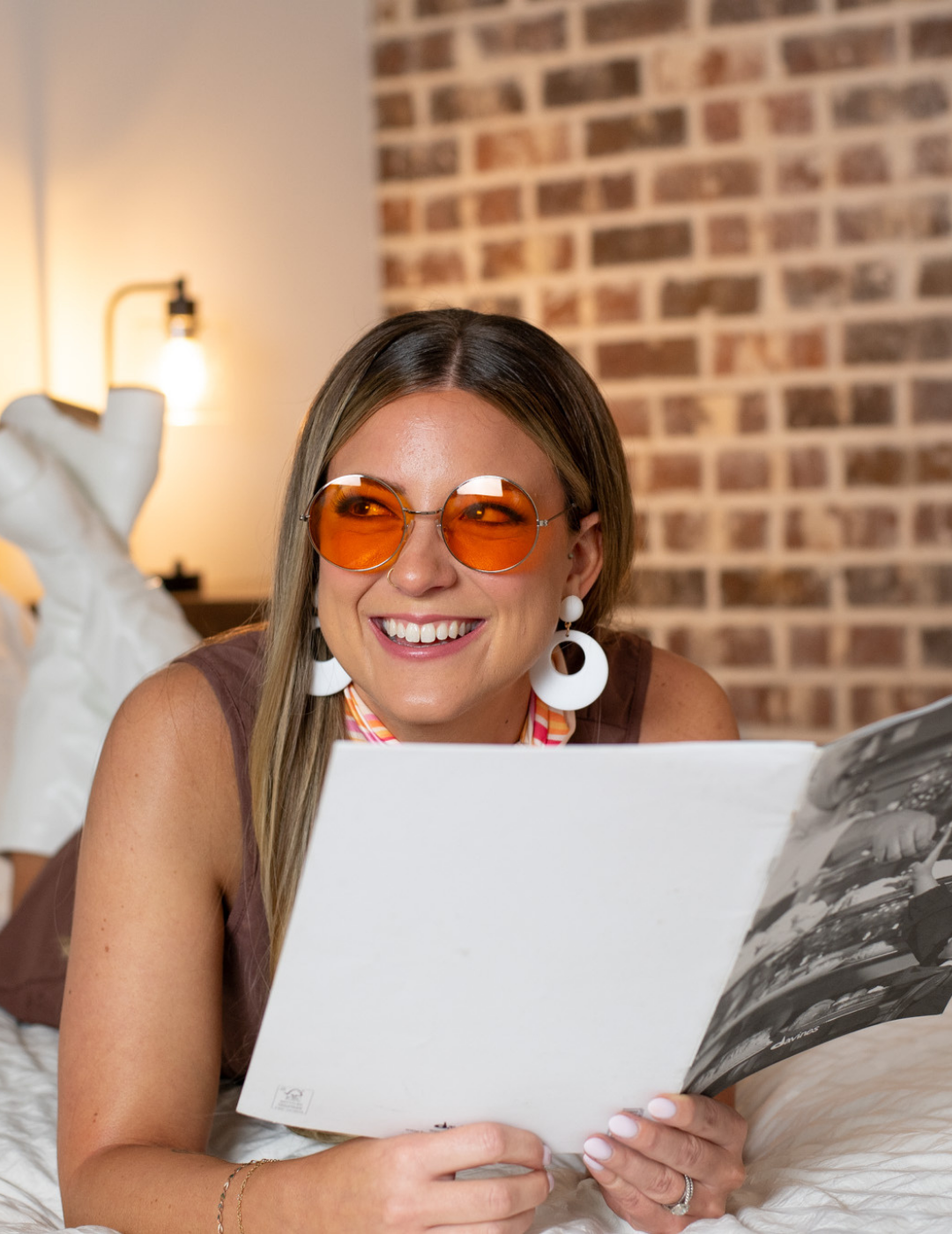 A smiling salon professional with orange-tinted glasses and white hoop earrings reviewing educational materials.