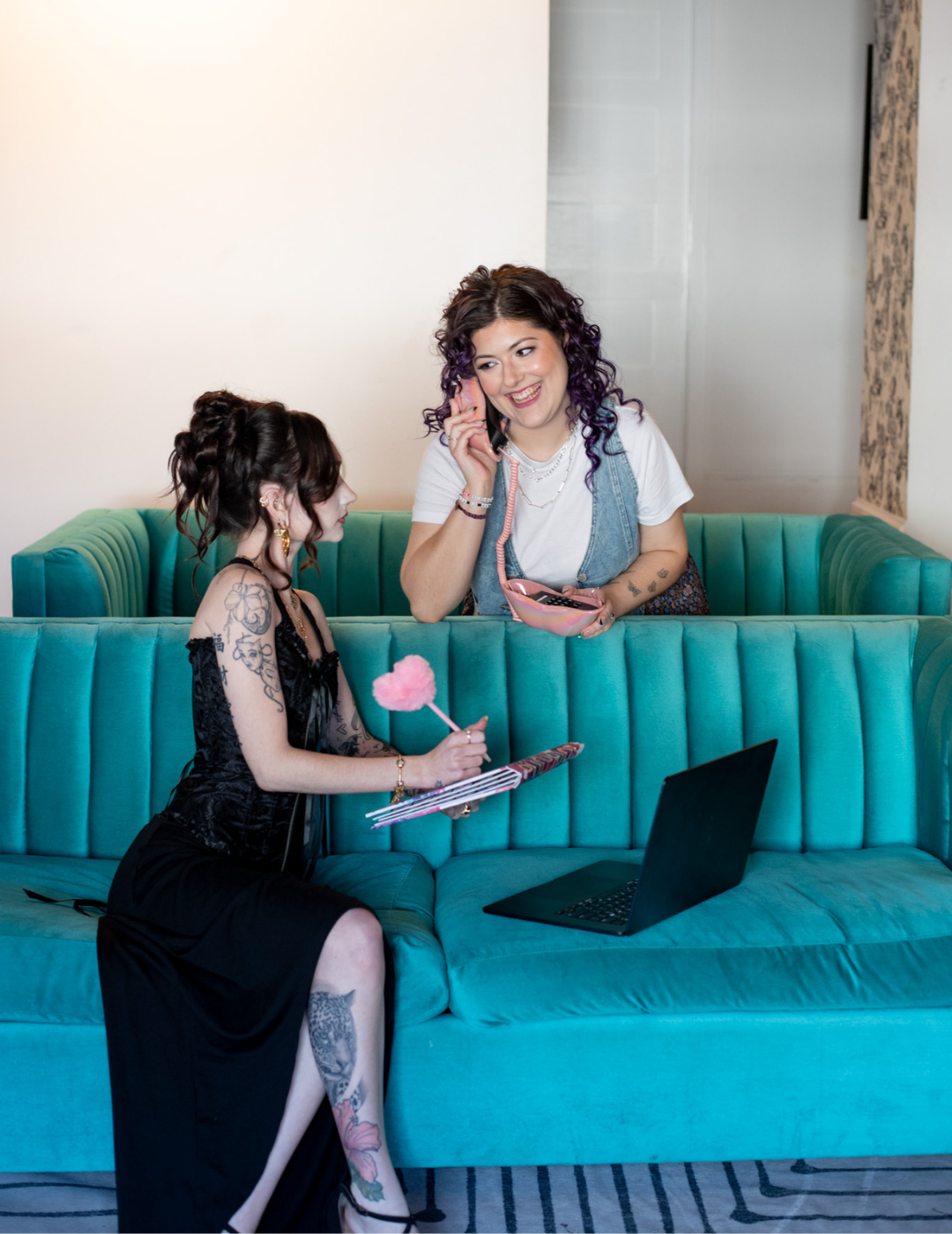 Two salon professionals, a manager and stylist, collaborating on a laptop in a modern salon with teal velvet seating at TW Salon.